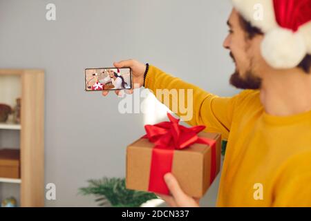 Jeune homme tenant un téléphone mobile, faisant un appel vidéo et montrant sa petite amie son cadeau de Noël Banque D'Images