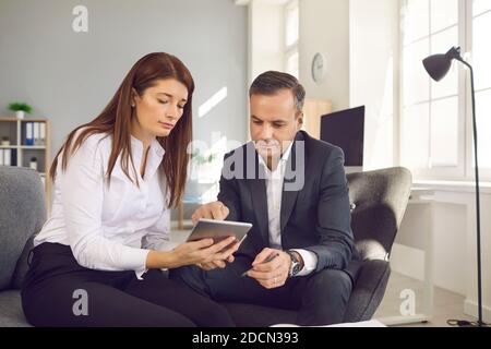 Les employés de bureau, hommes et femmes, sont assis sur une tablette numérique et vérifient les flux de travail au bureau. Banque D'Images