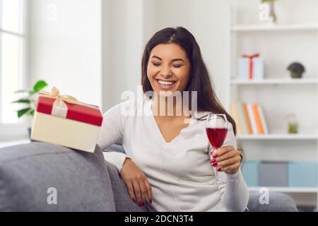 Rire jeune femme tenant un verre de vin ou de champagne pendant vidéo de célébration en ligne Banque D'Images