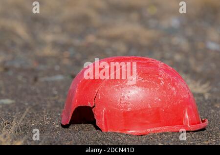 Un vieux casque cassé couché sur le sol. Il est un rouge décoloré et rayé, et il manque une pièce. Il est également fissuré. Il y a de la place pour te Banque D'Images