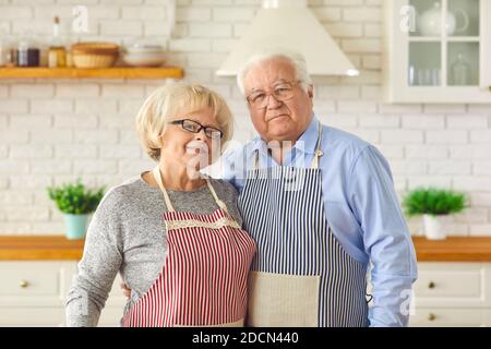 Portrait d'un heureux couple en tabliers dans la cuisine qui embrasse et regarde la caméra. Banque D'Images