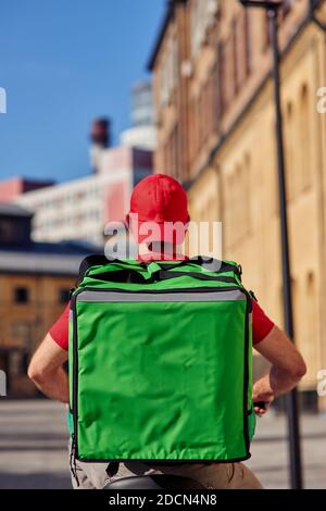 Vue arrière du liveur avec sac thermo à vélo le long de la rue sur une journée ensoleillée, vue verticale. Concept de service de livraison Banque D'Images