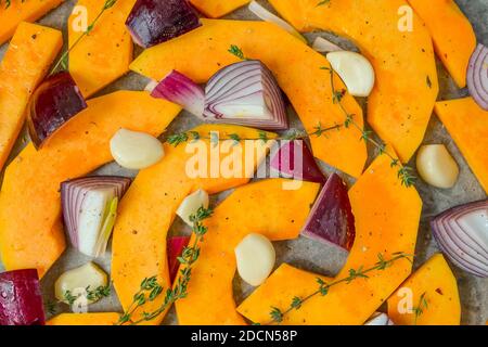 Des tranches de citrouille, des morceaux d'oignon rouge doux, de l'ail, des branches de thym et des épices sont préparés pour la cuisson. Concept d'alimentation saine. Orientation horizontale. S Banque D'Images