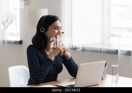 Femme d'affaires asiatique souriante portant un micro-casque/une oreillette sur un ordinateur portable, en regardant de côté Banque D'Images