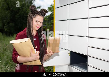 Une jeune fille prend soigneusement un paquet par paquet hors de la boîte aux lettres. Casier à colis automatique à Lublin. Les tresses africaines. Banque D'Images