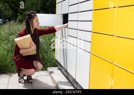 Une jeune fille prend soigneusement un paquet par paquet hors de la boîte aux lettres. Casier à colis automatique à Lublin. Les tresses africaines. Banque D'Images