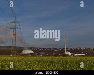 Centrale nucléaire exploitée par la société de services publics Energie Baden-Württemberg (EnBW) avec tour de refroidissement à vapeur et ligne électrique au-dessus du champ de colza. Banque D'Images