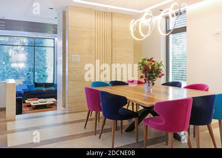 Salle à manger de luxe avec grande table en bois carrée, fleurs au milieu et dix chaises bleu marine et rose. Plafonniers modernes Banque D'Images