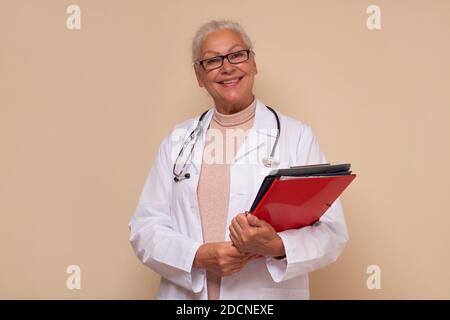 Femme médecin senior souriante avec stéthoscope autour du cou tenant des papiers. Prise de vue en studio Banque D'Images