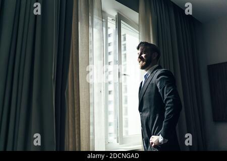 Un homme adulte avec une barbe en costume élégant debout près des fenêtres Banque D'Images