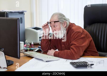 Homme âgé homme assis au bureau portant une chemise, ayant des difficultés ou des problèmes à utiliser l'ordinateur, regardant le moniteur Banque D'Images