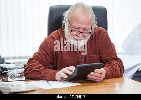 Un homme caucasien en âge de retraite compte sur une calculatrice assis à une table dans la salle de bureau Banque D'Images