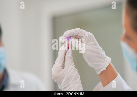 Femme technicien de laboratoire tenant un tube à essai avec un échantillon de sang d'une main et montrant la bonne façon de fermer la bouteille Banque D'Images