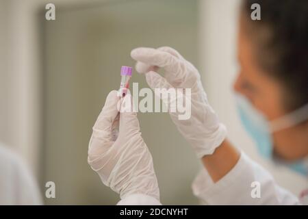 Femme technicien de laboratoire tenant un tube à essai avec un échantillon de sang d'une main et pointant vers le haut du flacon avec l'autre main Banque D'Images