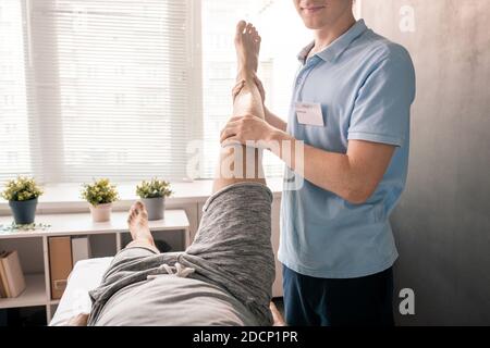 Physiothérapeute tenant la jambe du patient tout en l'aidant avec physique exercice Banque D'Images