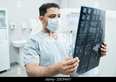 Radiologue masculin sérieux en masque et uniforme regardant la radiographie image du patient