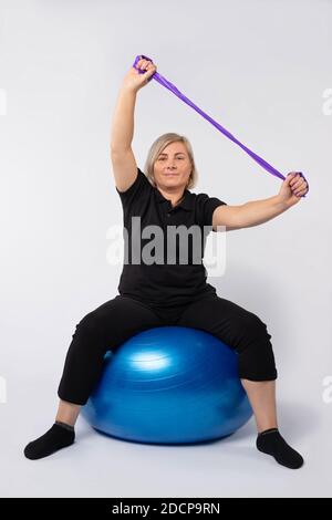 Femme âgée faisant de la maison de conditionnement physique en utilisant une balle et un élastique bande. Arrière-plan blanc. Banque D'Images