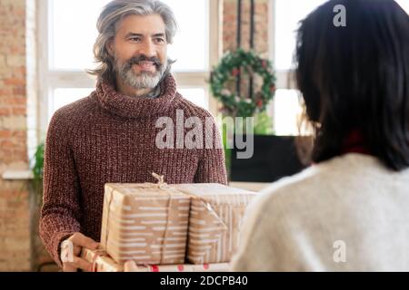 Un homme mûr heureux passant sa femme a emballé des boîtes-cadeaux tout en regardant à elle Banque D'Images