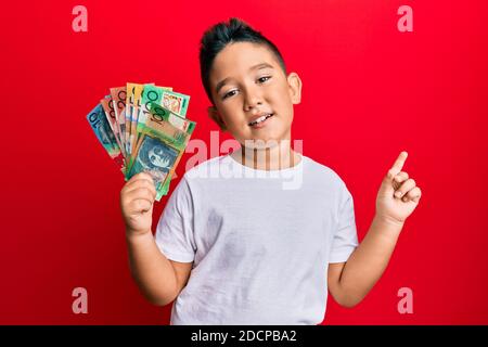 Petit garçon hispanique enfant tenant des dollars australiens sourire heureux pointant avec la main et le doigt sur le côté Banque D'Images