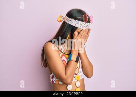 Belle femme hispanique portant le style bohème et hippie avec l'expression triste couvrant le visage avec les mains en pleurant. Concept de dépression. Banque D'Images