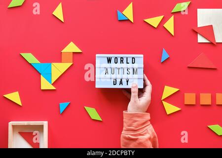 Design créatif pour la Journée mondiale de l'autisme le 2 avril, texte sur la visionneuse. Des éléments de puzzle Tangram dispersés sur fond rouge. Boîtier d'éclairage à main. Banque D'Images