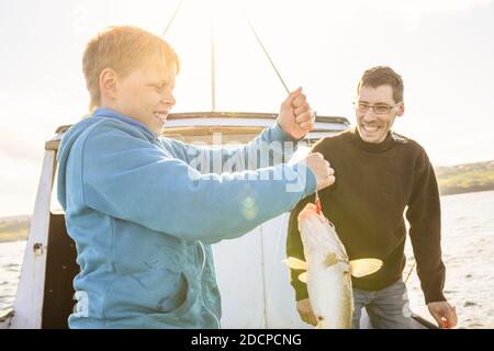 Adolescent debout avec du poisson pêché sur le bateau avec sourire père pendant la pêche Banque D'Images