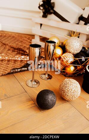 Deux verres à boire en métal or sur parquet avec décorations pour Noël dans des tons or et noir: Balles rondes brillantes, boîtes-cadeaux, guirlandes et SH Banque D'Images