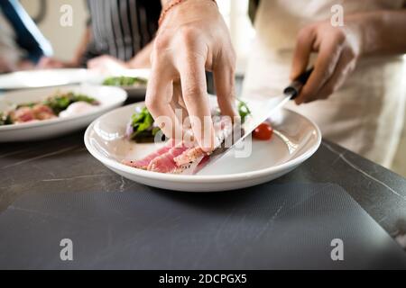 Mains de jeune homme dans le tablier mettant morceau de fumé ou du bœuf grillé sur l'assiette Banque D'Images