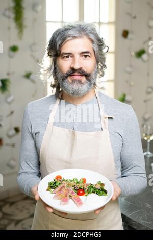 Homme barbu mature en pull-over et plateau de maintien avec salade de légumes Banque D'Images