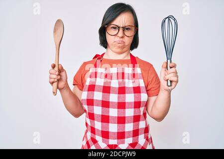 Brunette femme avec le syndrome de Down cuisson à l'aide du fouet boulanger et de la cuillère sceptique et nerveux, frowning bouleversé à cause du problème. Personne négative. Banque D'Images