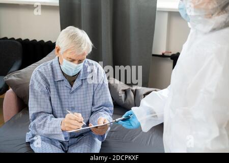 Malade senior homme patient dans le masque et le pyjama signature médicale papier sur la table Banque D'Images