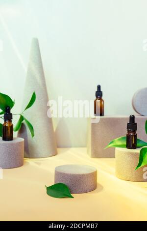 Arrière-plan tendance de formes géométriques avec des bouteilles d'huiles essentielles naturelles, des feuilles fraîches et un podium central vide pour la présentation des produits. Beauté et Banque D'Images