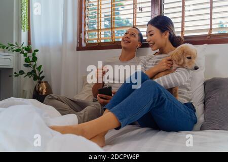 Portrait d'un jeune adulte asiatique heureux sur le lit avec un animal de compagnie dans la scène intérieure de la chambre. L'homme et la femme écoutent la musique ensemble. Concept de vie de mariage et de relation heureuse Banque D'Images