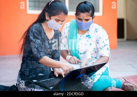 Deux jeunes filles collégiales étudiants en masque médical de travail ou d'étude de projet sur ordinateur portable à l'université - concept de l'université de rouvrir, nouvelle normale en raison de corona Banque D'Images