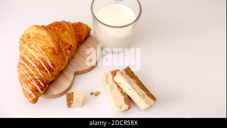 Grand croissant et tasse en verre avec support à lait sur un table blanche Banque D'Images