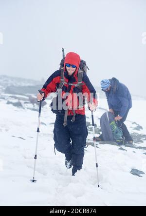 Jeune homme touriste marchant dans la neige tout en un ami qui se déchillait dans un sac à dos. Randonneur masculin avec bâtons de randonnée portant des lunettes de soleil et une veste de sport à capuche. Concept de voyage, de randonnée et d'alpinisme. Banque D'Images