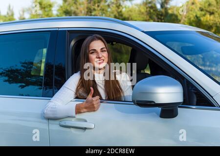 Une jeune fille regarde par la fenêtre d'un blanc voiture souriant et montre sa main tout est bien Banque D'Images