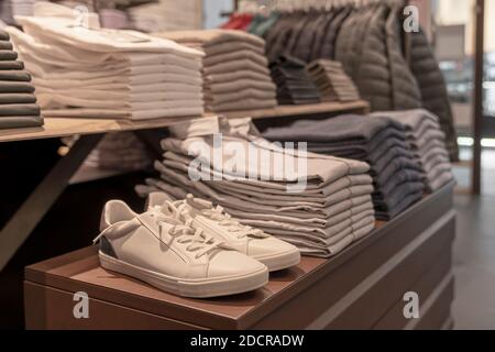 magasin de vêtements pour hommes - baskets, chemises et vestes blanches et grises avec chandail, accrochées dans un ensemble et empilées dans un style élégant. Banque D'Images