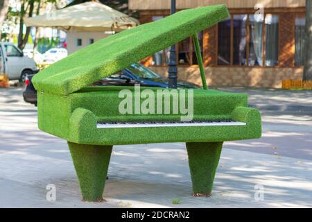 Sculpture d'un piano à queue avec couvercle ouvert en herbe artificielle, topiaire urbaine. Banque D'Images