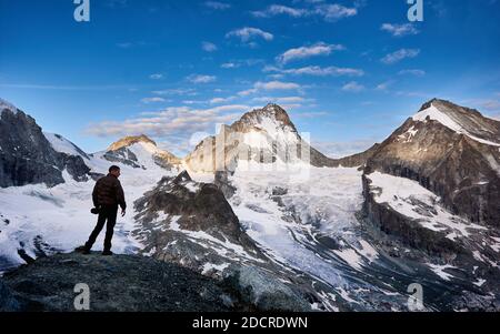 Voyageur masculin accueillant un nouveau jour dans les Alpes suisses, le soleil lumineux du matin brille aux sommets, Dent Blanche, tandis que la vallée est encore dans l'ombre Banque D'Images