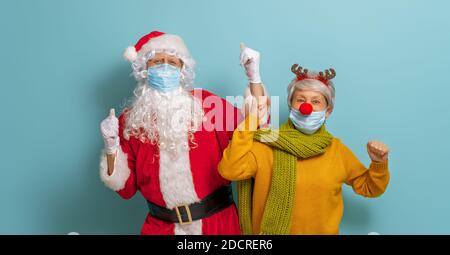 Joyeux Noël et joyeuses fêtes ! Le Père Noël et le renne sur fond de couleur vive. Personnes âgées en costumes de carnaval portant des masques de visage pendant Banque D'Images