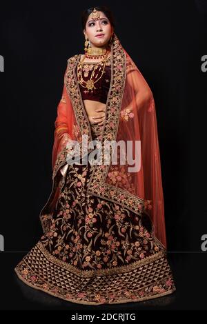 Jeune femme indienne attrayante modèle habillé en costume traditionnel indien lehenga choli avec des bijoux de style Kundan. Prise de vue en longueur. Arrière-plan noir Banque D'Images