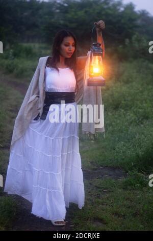 Femme en robe blanche avec lanterne rétro éclairée à l'extérieur nuit Banque D'Images