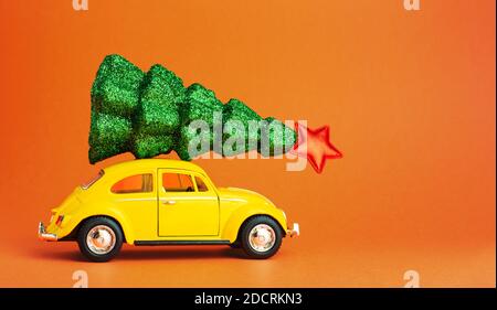 Voiture de jouet rétro jaune portant un arbre de noël festif sur le toit. Arbre du nouvel an sur le toit de la voiture. Arrière-plan de couleur orange avec espace de copie miniature créative Banque D'Images