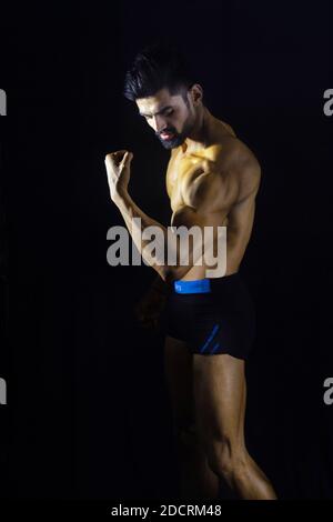 Un homme musclé de bodybuilder en salle de sport. Fond noir. Profil latéral. Regarder vers le bas. Affichage de gros biceps Banque D'Images