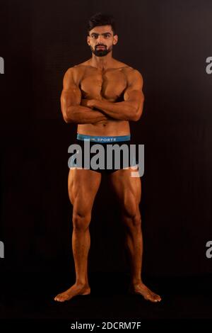 Un homme musclé de bodybuilder en salle de sport. Arrière-plan noir. Profil avant. Regarder l'appareil photo. Prise de vue en longueur Banque D'Images