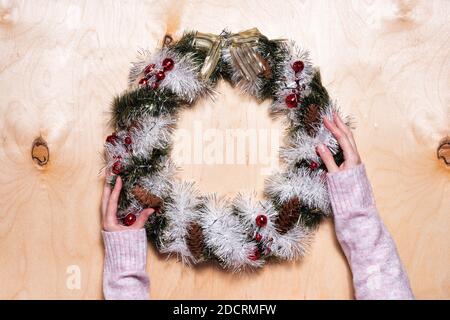 Guirlande scintillante de Noël avec cône, baies rouges et noeud doré aux mains des femmes sur fond de bois Banque D'Images