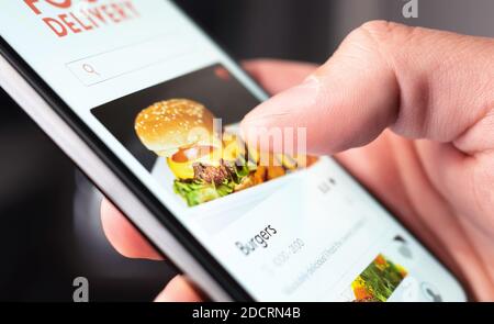 Commande d'application de livraison de nourriture avec téléphone. Service mobile en ligne pour les hamburgers et les pizzas à emporter. Homme affamé lisant le menu du restaurant, le site Web et les commentaires. Banque D'Images