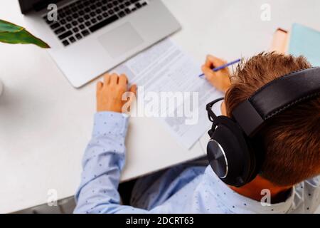 Un homme d'école fait ses devoirs à la maison, assis à un bureau avec un ordinateur portable. Enseignement à distance, quarantaine, coronavirus Banque D'Images