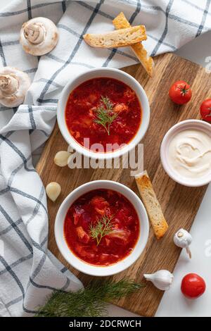 Vue de dessus du traditionnel borscht ukrainien ou soupe avec betteraves, pommes de terre, tomates, viande dans des bols sur fond blanc. Vue de dessus. Espace de copie libre. Banque D'Images